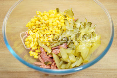 Добавить в миску нарезанные соломкой огурцы и кукурузу.