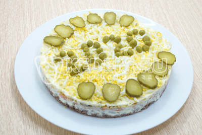Украсить салат маринованными огурчиками и зеленым горошком. Снять сервировочное кольцо.