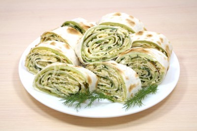 Разрезать рулет из лаваша с огурцом и сыром на порционные кусочки и выложить на блюдо.