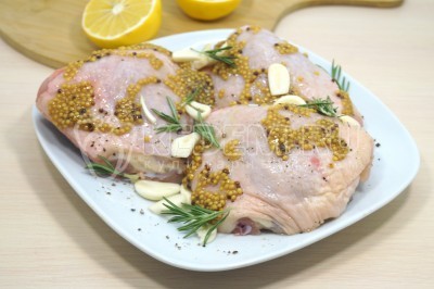 Добавить к курице чеснок и розмарин. Обмазать куриные бедра 2 столовыми ложками горчицы с зернами. Выжать сок половинки лимона сверху и оставить мариноваться на 30 минут.