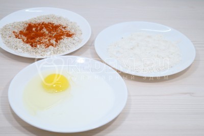 Приготовить три плоские тарелки: в одной смешать яйцо и 2 столовые ложки молока, на вторую выложить 3 столовые ложки муки и на третьей тарелке - хлопья с паприкой.