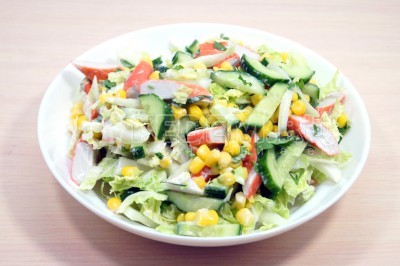 Выложить салат с крабовыми палочками, пекинской капустой, огурцами и кукурузой в салатницу.