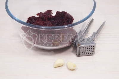 Остывшую свёклу очистить. Натереть свеклу на терке в миску. Добавить 2 прессованных зубчика чеснока.
