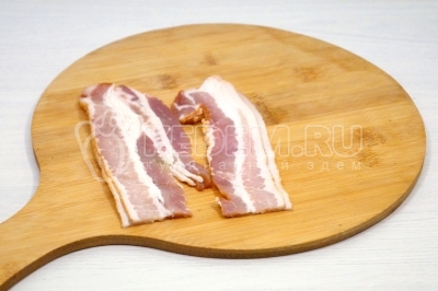 Чтобы приготовить скрэмбл с беконом на завтрак, нужно две полоски сырокопченого бекона разрезать на половинки.