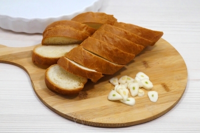 Чтобы приготовить камамбер запеченный в духовке с багетом, нужно багет нарезать ломтиками, 2 зубчика чеснока нарезать тонкими ломтиками.